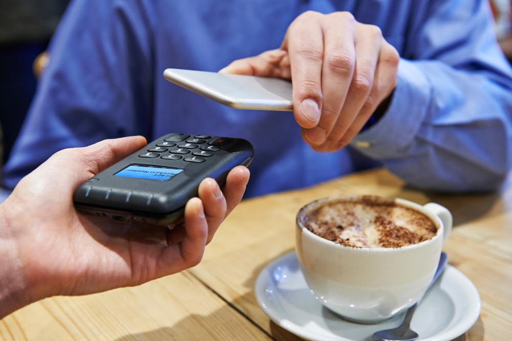 Man Using Contactless Payment App On Mobile Phone In Cafe