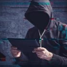 Latest Ransomware Exploit Shows Importance Of Up-To-Date Cybersecurity Cyber crime concept with digital glitch effect depicting faceless hooded person with digital tablet computer hacking online accounts