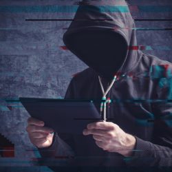 Latest Ransomware Exploit Shows Importance Of Up-To-Date Cybersecurity Cyber crime concept with digital glitch effect depicting faceless hooded person with digital tablet computer hacking online accounts