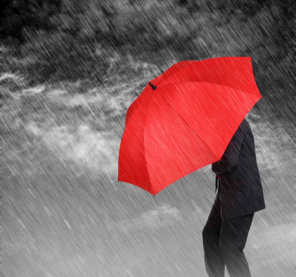 Businessman with red umbrella protecting himself from the storm concept for protection from recession or economic depression etc