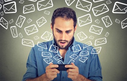 Important: IOL, EsatClear & OceanFree Email Closeup portrait young shocked man busy sending messages emails from smart phone email icons flying of mobile phone isolated on gray wall background. Telecommunications, internet, data plan concept